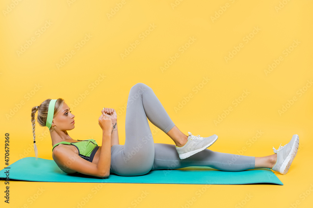 side view of woman in grey leggings and green sports bra exercising on fitness mat on yellow side view of woman in grey leggings and green sports bra exercising on fitness mat on yellow