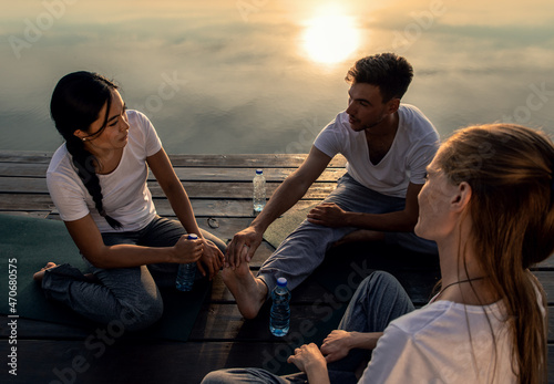 Group of people talking after yoga exercises by the lake at sunset.