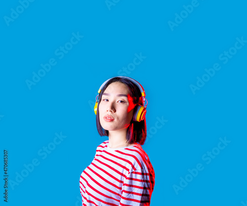 Portrait young asiatic woman wearing wireless bluetooth headphones listening music looking camera isolated advertising copyspace background