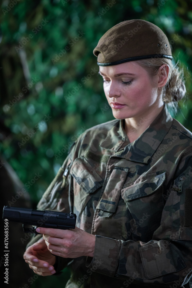 A lady soldier watches and inspects a gun. A soldier in full uniform.