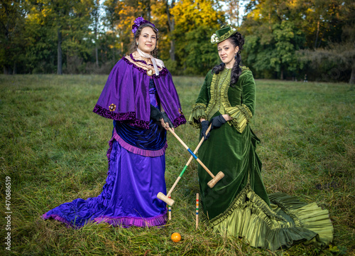 Women in 19th century costumes play croquet in the city park