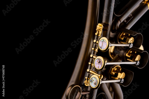 A rotary type trumpet with a curved leadpipe in matte brown with gold elements and pearl type buttons on a black background