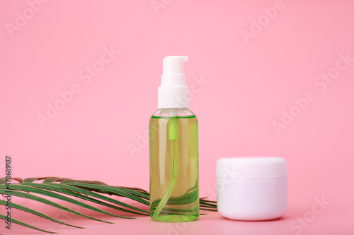 Close up of green cleansing gel or foam for face and cosmetic jar with cream, balm or mask on pink background with palm leaf. Concept of organic cosmetics for daily skin care routine