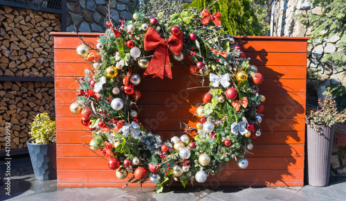A large ring made of spruce branches, decorated with white and red balls on a red plank background as a design option for the Christmas and New Year holidays