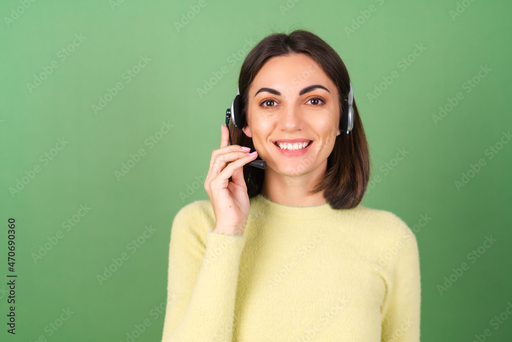 Young woman on a green background in a yellow sweater manager, support service worker, salesperson, with pleasure accepts calls from customers Young woman on a green background in a yellow sweater manager, support service worker, salesperson, with pleasure accepts calls from customers
