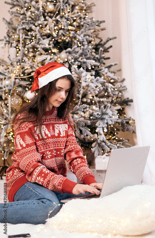 Young woman buying online at home for winter holidays using laptop computer. Christmas holiday shopping on a christmas tree background Young woman buying online at home for winter holidays using laptop computer. Christmas holiday shopping on a christmas tree background