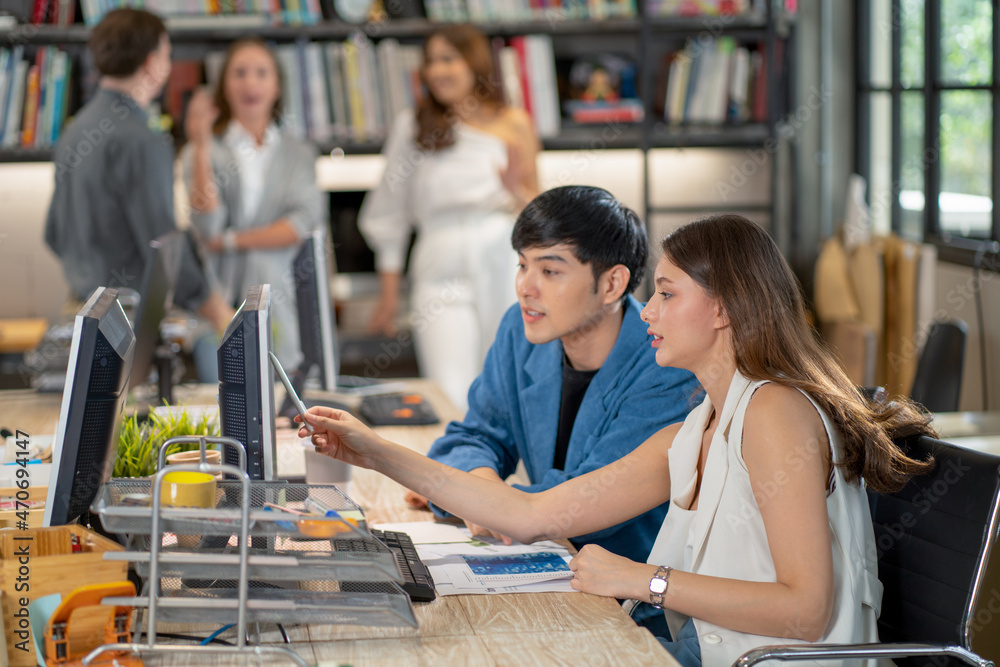 Beautiful woman point to monitor and discuss with co-worker in office with other stay in background and talk together. Beautiful woman point to monitor and discuss with co-worker in office with other stay in background and talk together.