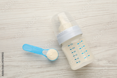 Feeding bottle with infant formula and powder on white wooden table, flat lay