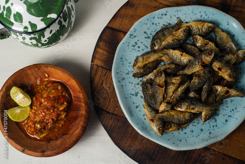 fried baby fish with hot and spicy sauce and cantella asiatica as side dish on wooden board against white background photo