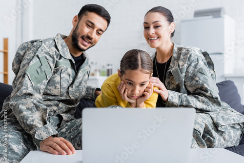 Kid looking at laptop near blurred parents in military uniform on couch © LIGHTFIELD STUDIOS