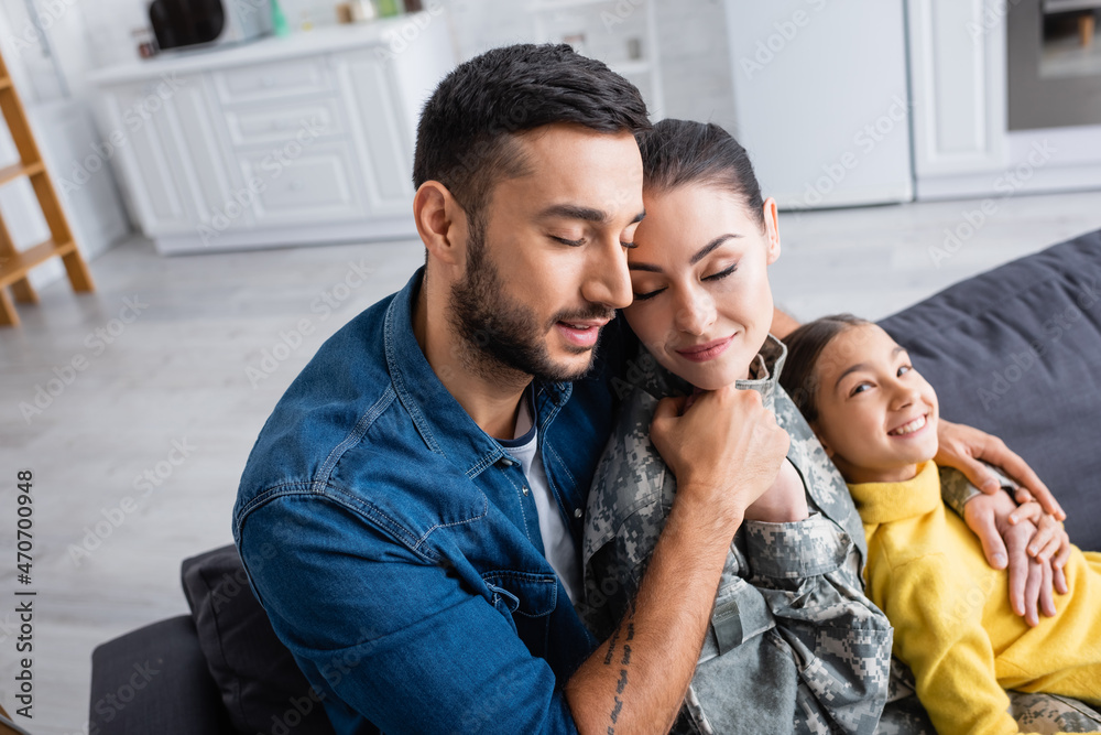Man embracing wife in military uniform near child on couch at home Man embracing wife in military uniform near child on couch at home