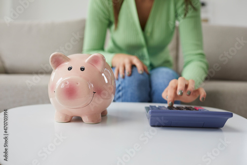 Close up of woman calculate finances on machine consider family budget. Female count expenses expenditures on calculator think of savings in piggy bank. Money planning. Financial investment.