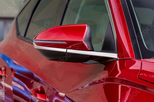 Close up front view of car side mirror. Front rear view mirror on the car window. Car exterior details. Red car mirror.
