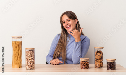 Young caucasian woman sitting at a table with food pot isolated on white background showing a mobile phone call gesture with fingers.