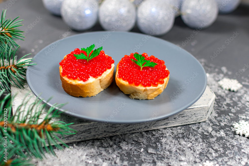 Sandwiches with red caviar on a gray plate on a stone table against the background of a Christmas tree and Christmas balls. Christmas, New Years holidays. Festive food. Sandwiches with red caviar on a gray plate on a stone table against the background of a Christmas tree and Christmas balls. Christmas, New Years holidays. Festive food.