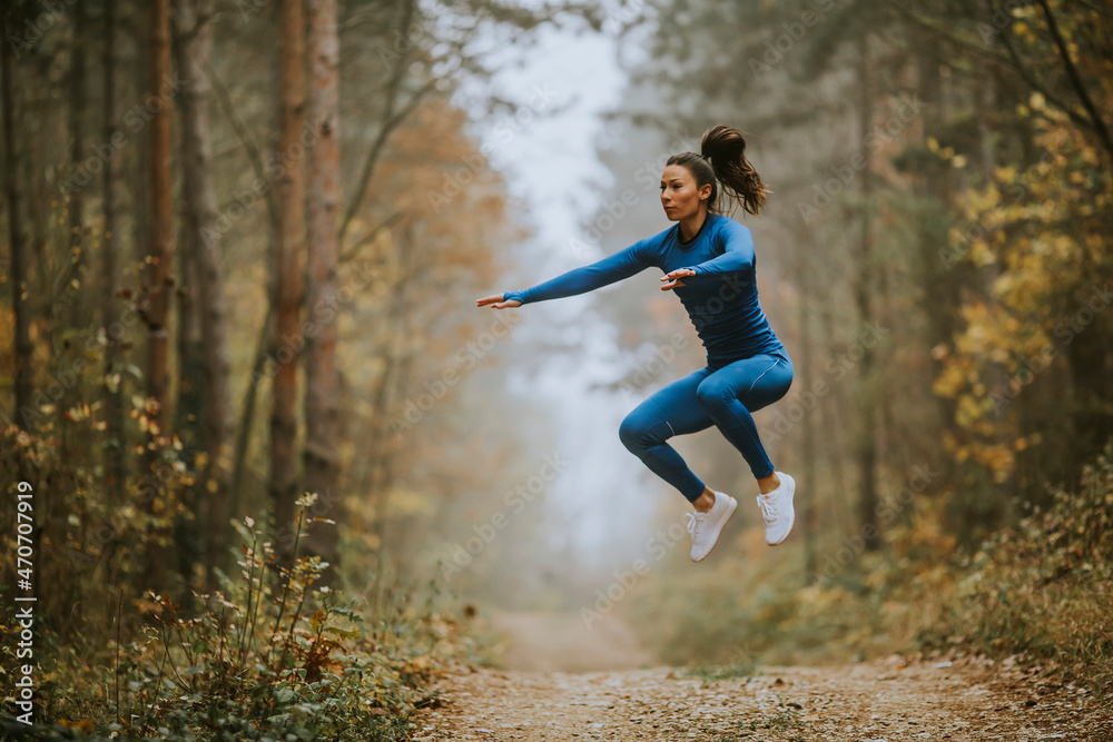 Young woman taking high jump on the forest trail at autumn