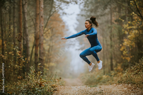 Young woman taking high jump on the forest trail at autumn