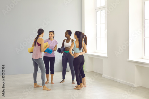 Smiling diverse gen Z females in sportswear laugh talk chat after morning stretching pilates class in fitness club. Happy multiracial women girls speak at workout or training session. Sport concept.