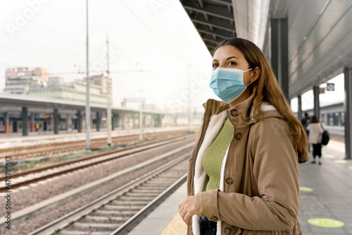 Beautiful woman in a medical mask waiting train on station. Portrait of a young woman with a surgical mask on her face against SARS-cov-2 outdoors. photo