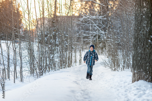 A cheerful and handsome boy in blue clothes runs along a snow-covered path in the park. Winter activities.