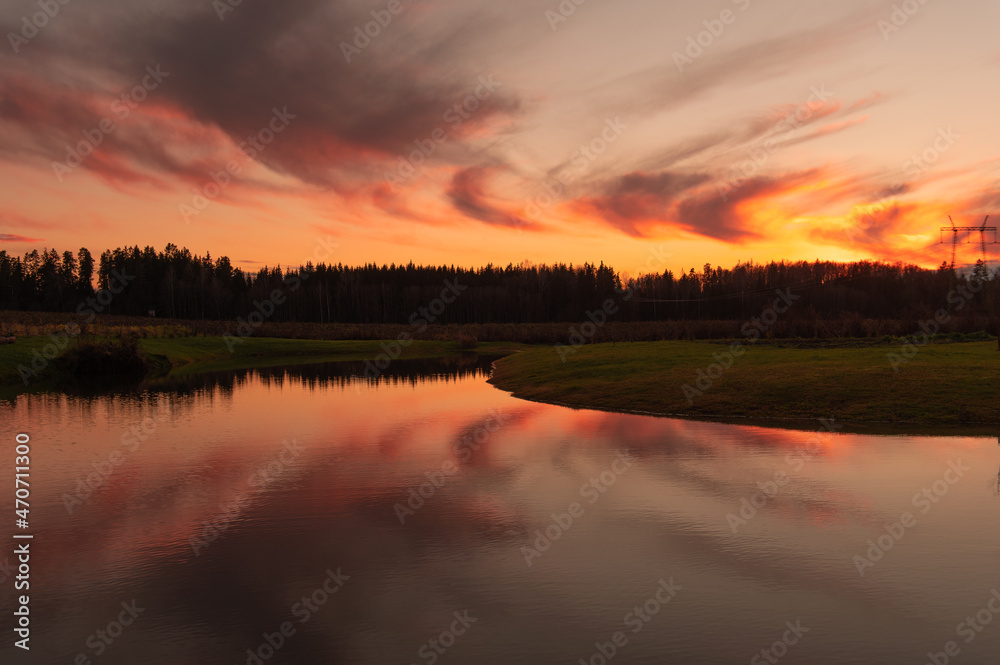 reflections of colored clouds in the lake water at sunset,silhouettes of trees in golden hour