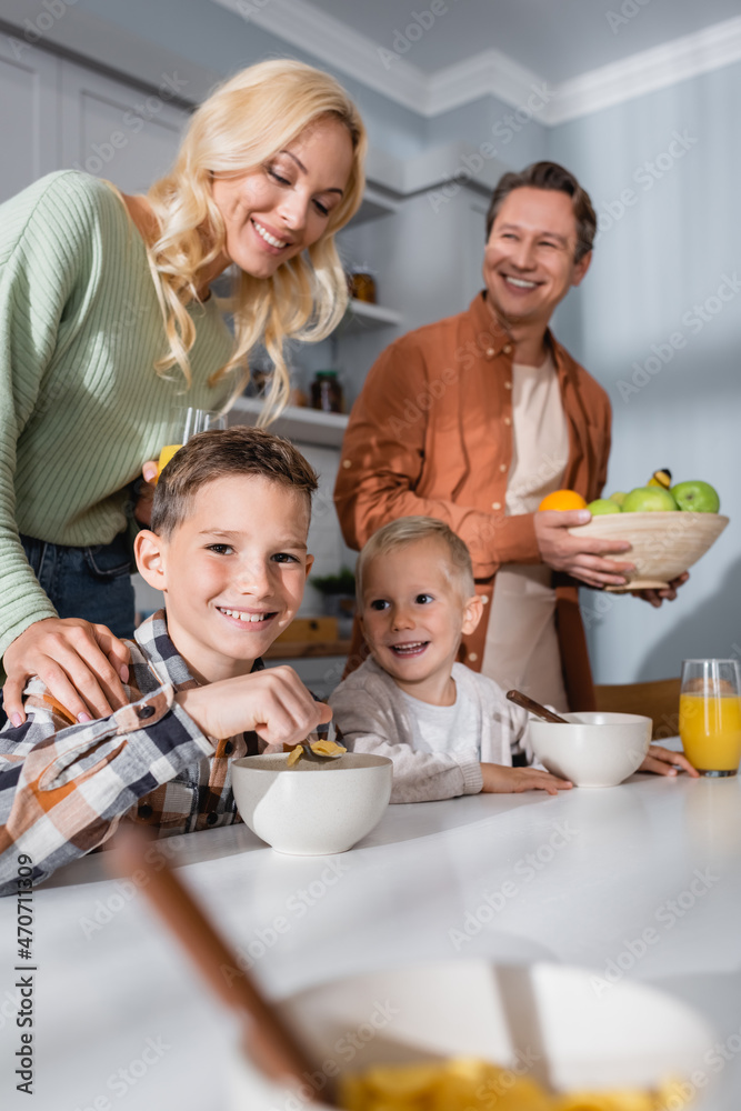 happy brothers eating corn flakes near happy parents in kitchen happy brothers eating corn flakes near happy parents in kitchen