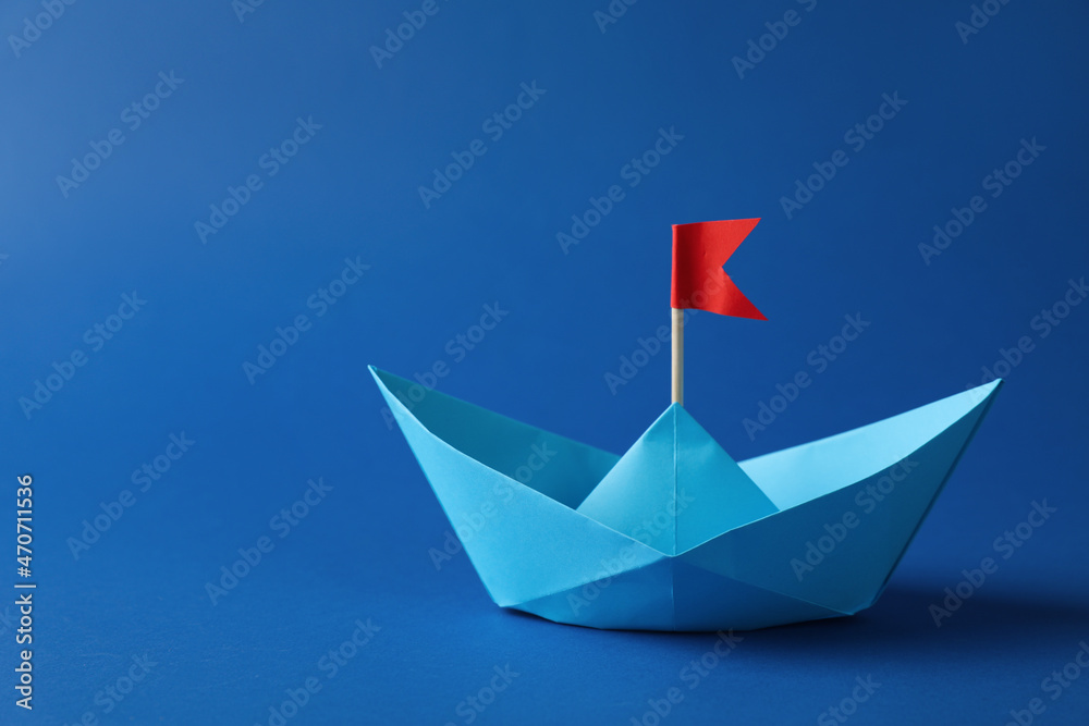 Handmade paper boat with red flag on blue background. Space for text. Origami art Handmade paper boat with red flag on blue background. Space for text. Origami art