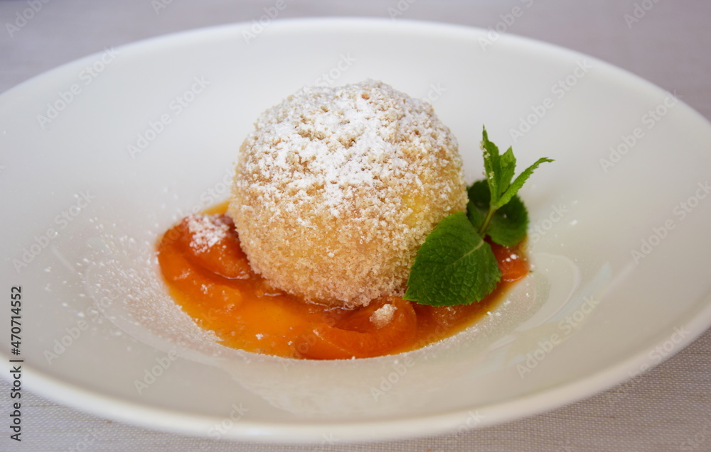 Marillenknödel mit Marillenröster, Staubzucker und Semmelbrösel auf weißen Teller. Traditionelle Nachspeise aus Südtirol und Österreich Marillenknödel mit Marillenröster, Staubzucker und Semmelbrösel auf weißen Teller. Traditionelle Nachspeise aus Südtirol und Österreich