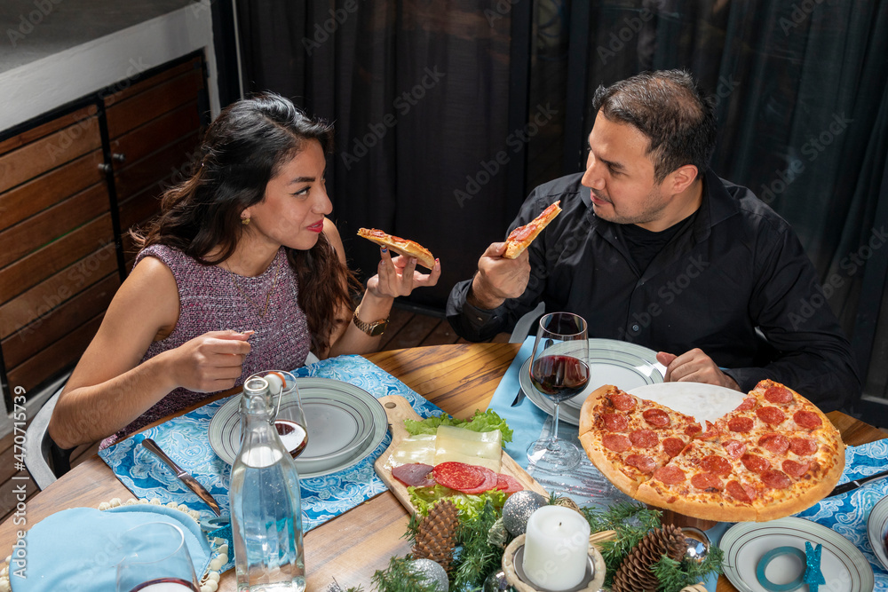 couple eating pizza while looking into each other's happy eyes during christmas dinner