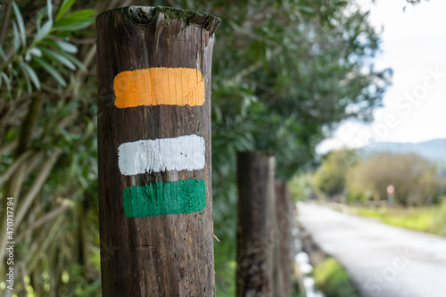 Close-up to a wooden post with stripes painted in orange, white and green colors. It is used to mark paths and trails in nature.