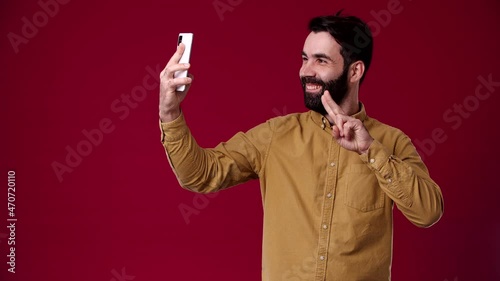 the guy got a video call, he is very happy about it, he laughs, black-haired, bearded, dressed in a brown shirt, the background is red