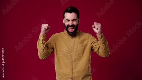 the guy counts to 3 and waves his hands with joy, smiles, new year, birthday, he is bearded, dark-haired, dressed in a brown shirt, the background is red
