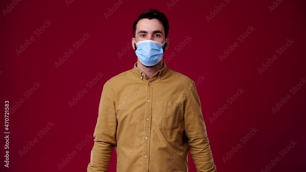 a man puts on a mask, protection from the virus, pandemic, he is black-haired, bearded, dressed in a brown t-shirt, the background is red a man puts on a mask, protection from the virus, pandemic, he is black-haired, bearded, dressed in a brown t-shirt, the background is red