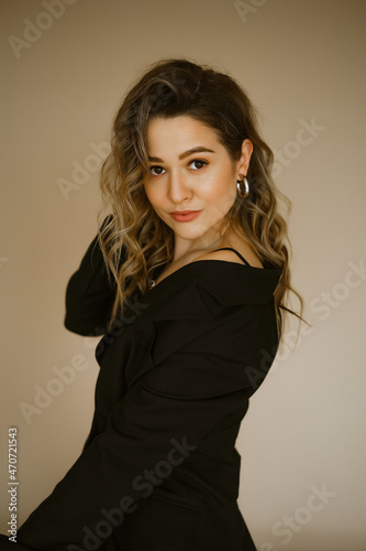 portrait of young beauty caucasian woman in a black suit , a girl with makeup and curly hair in jacket, a dark eyes lady with earrings-rings and bright makeup on light background