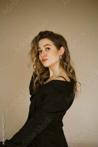 portrait of young beauty caucasian woman in a black suit , a girl with makeup and curly hair in jacket, a dark eyes lady with earrings-rings and bright makeup on light background