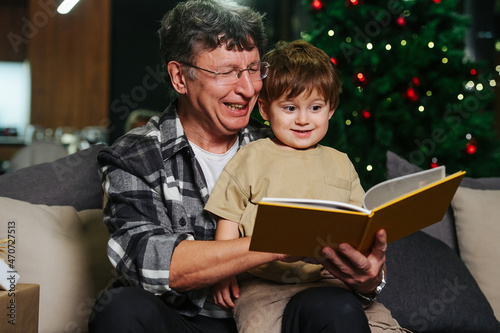 Mesmerized boy and grandpa looking through photo album next to christmas tree