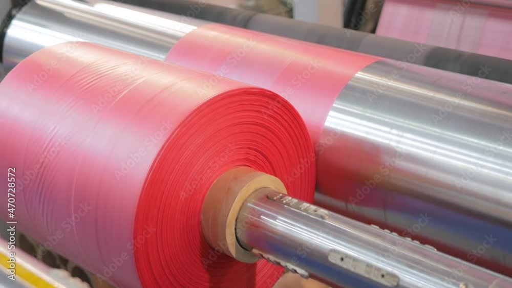 Close up: moving roller with flat polyethylene pink film - automatic plastic bag making machine at exhibition, trade show. Recycling, manufacturing, industry, automated technology equipment concept