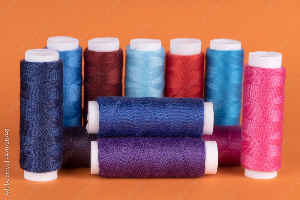 Bobbins of sewing thread of different colors isolated on orange Bobbins of sewing thread of different colors isolated on orange