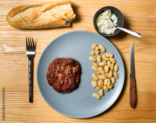 Tasty grilled burger served with coocked vegetarian beans in a plate on a rustic wooden table. Flat lay, top view photo