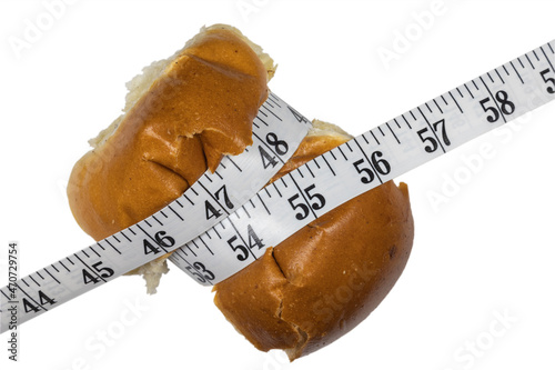 Bun compressed with measuring tape. The concept of willpower when losing weight. Weight and diet control. Bun on white background.
