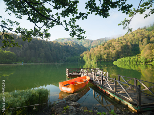 Pier and orange boat on the lake. Landscape of an mountain lake in front of mountain range. 
