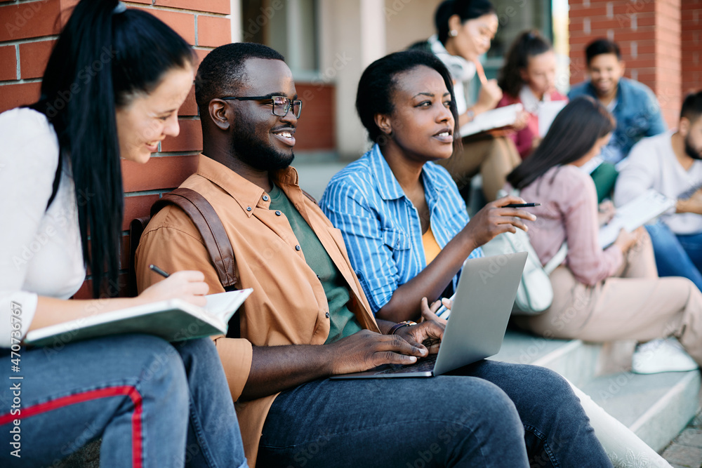 Happy black student using laptop while learning with his friends at campus. Happy black student using laptop while learning with his friends at campus.