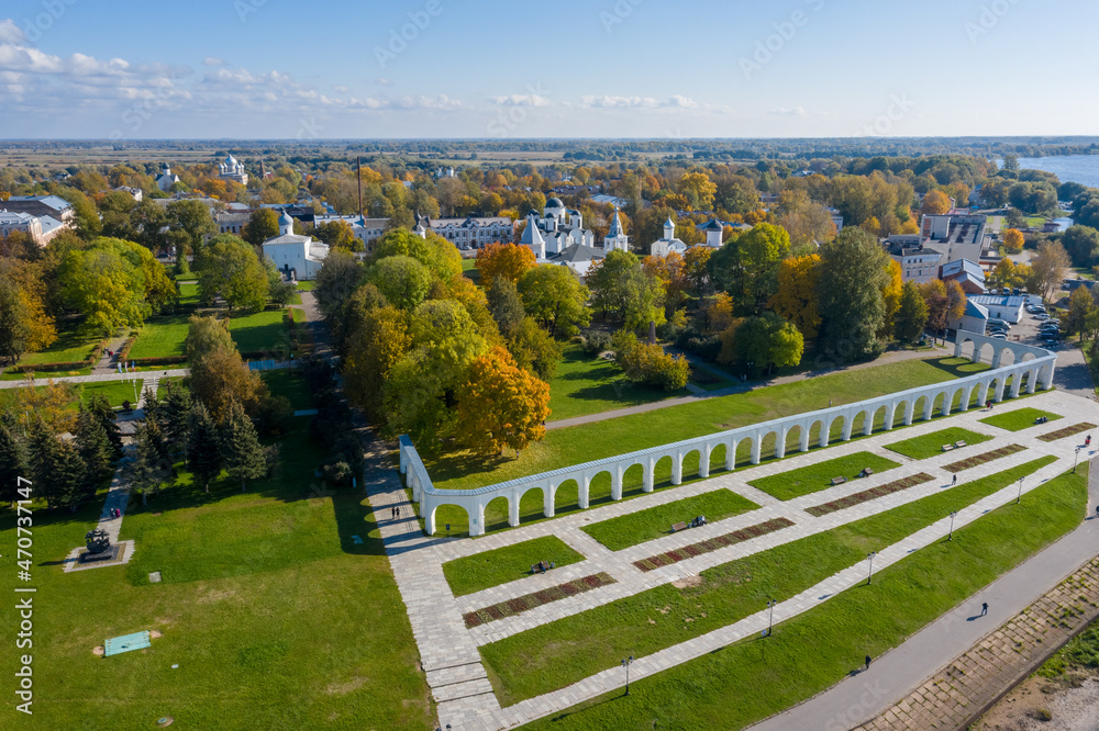 Panoramic aerial view of the Gostiny Dvor Arcade in Veliky Novgorod, autumn treetops on a sunny day. Remaining ruins of a medieval market. Monument to the heroes.