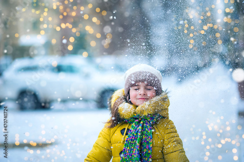 Happy girl in yellow jacket plays with snow. Children games in winter..