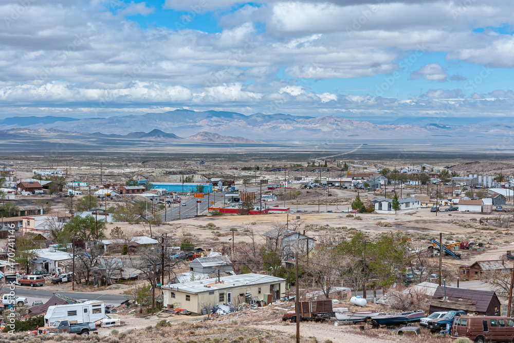 Tonopah, Nevada, US - May 18, 2011: Wide view over part of town bordering flat desert. Mountain range on horizon under blue cloudscape. Sprinkled housing in front with hotel and casino.