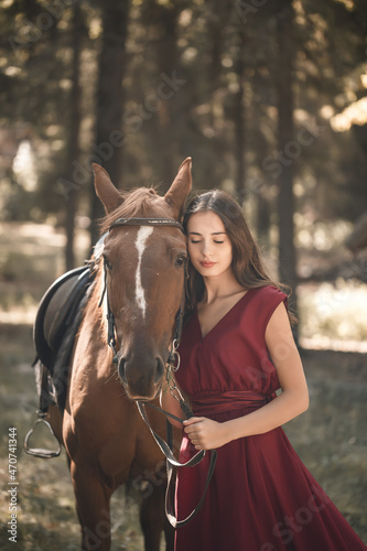 Portrait of a smiling young woman hugging her brown horse. A girl in a dress is standing near a horse. The concept of friendship between people and pets.