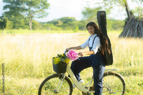 Adorable smiling young girl on a bicycle with a guitar on her back in the field
 photo