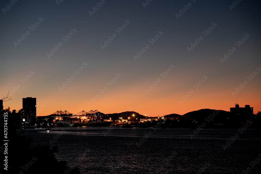 Sunset in the city with buildings and ships harbor, sea, river and sky. City at night.