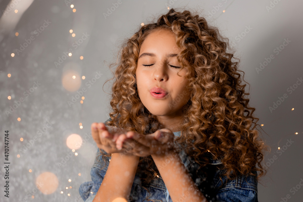 girl with blue eyes and light curly hair blows artificial snow from her palms. holiday goods. young woman celebrates the onset of winter. space for text. High quality photo