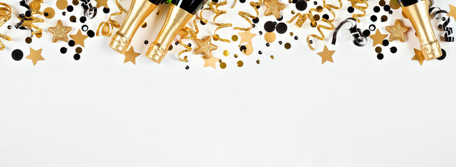 New Years Eve top border of gold and black confetti, streamers and champagne. Overhead view over a white banner background.